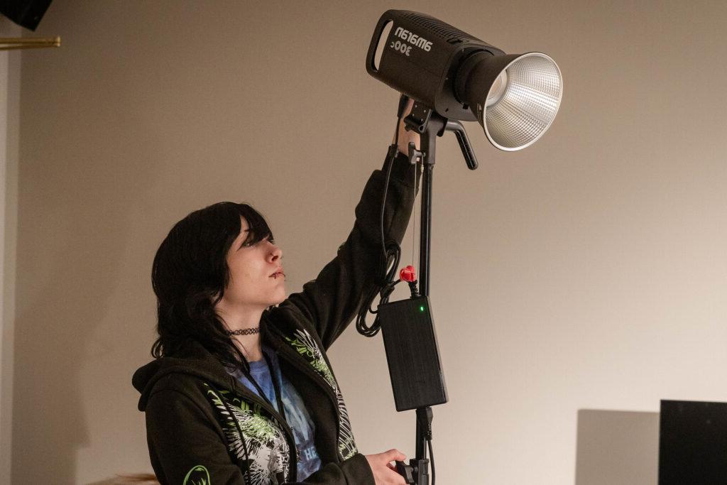 Student adjusts lights on a film set.