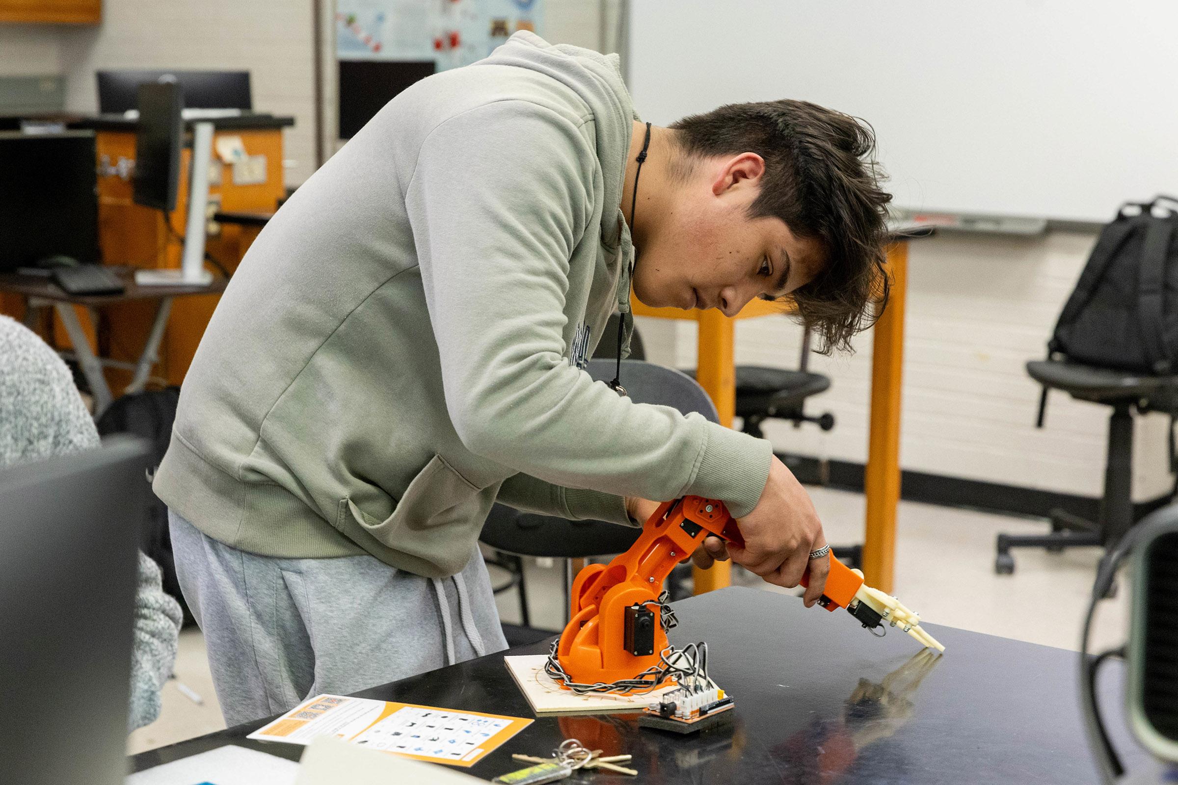 A Randolph College engineering student assembles a robotic arm in a lab session.