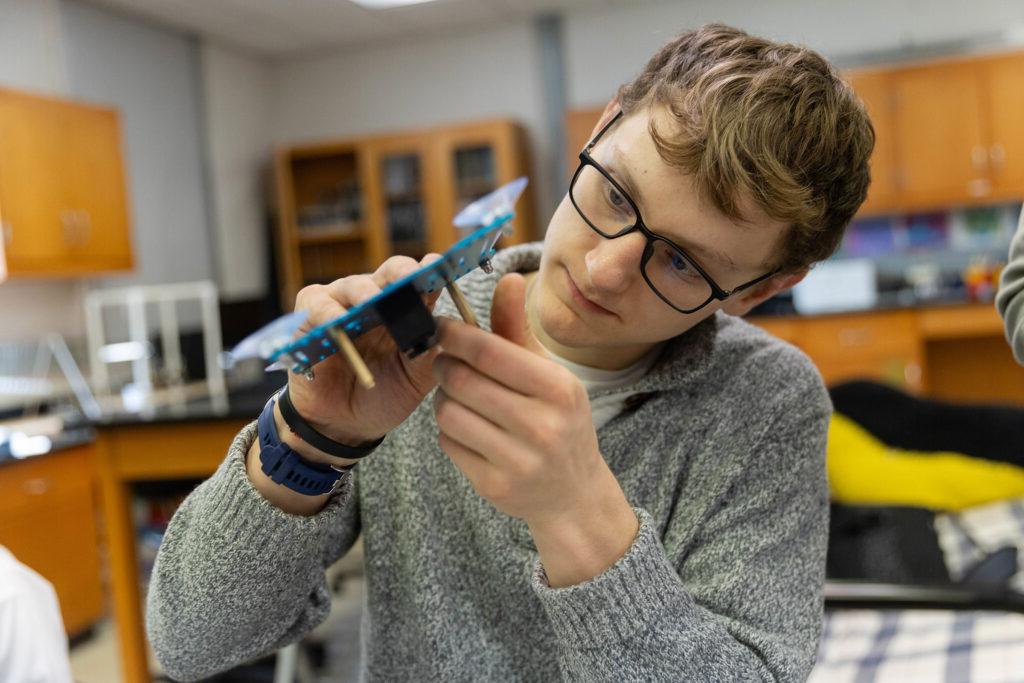 Randolph College student makes adjustments to a part on a robotic arm.